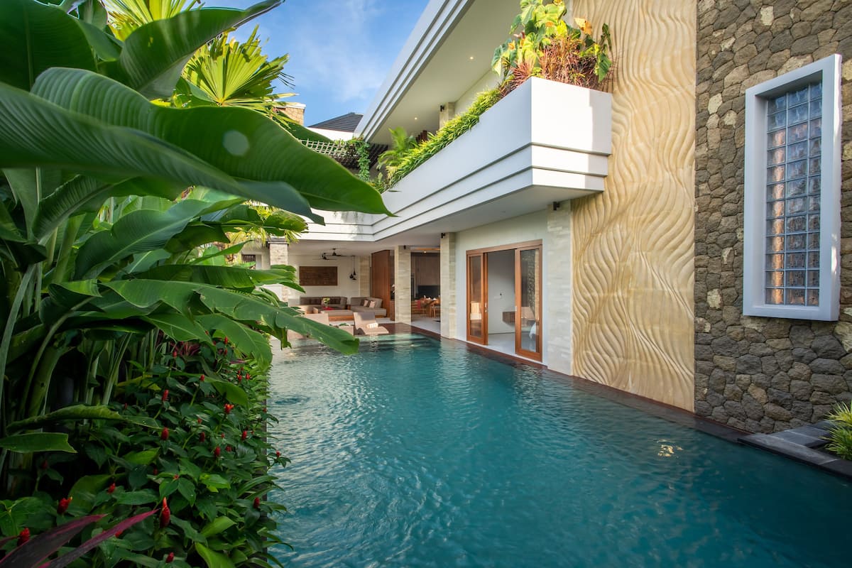 A modern pool area with a stone wall and lush greenery.