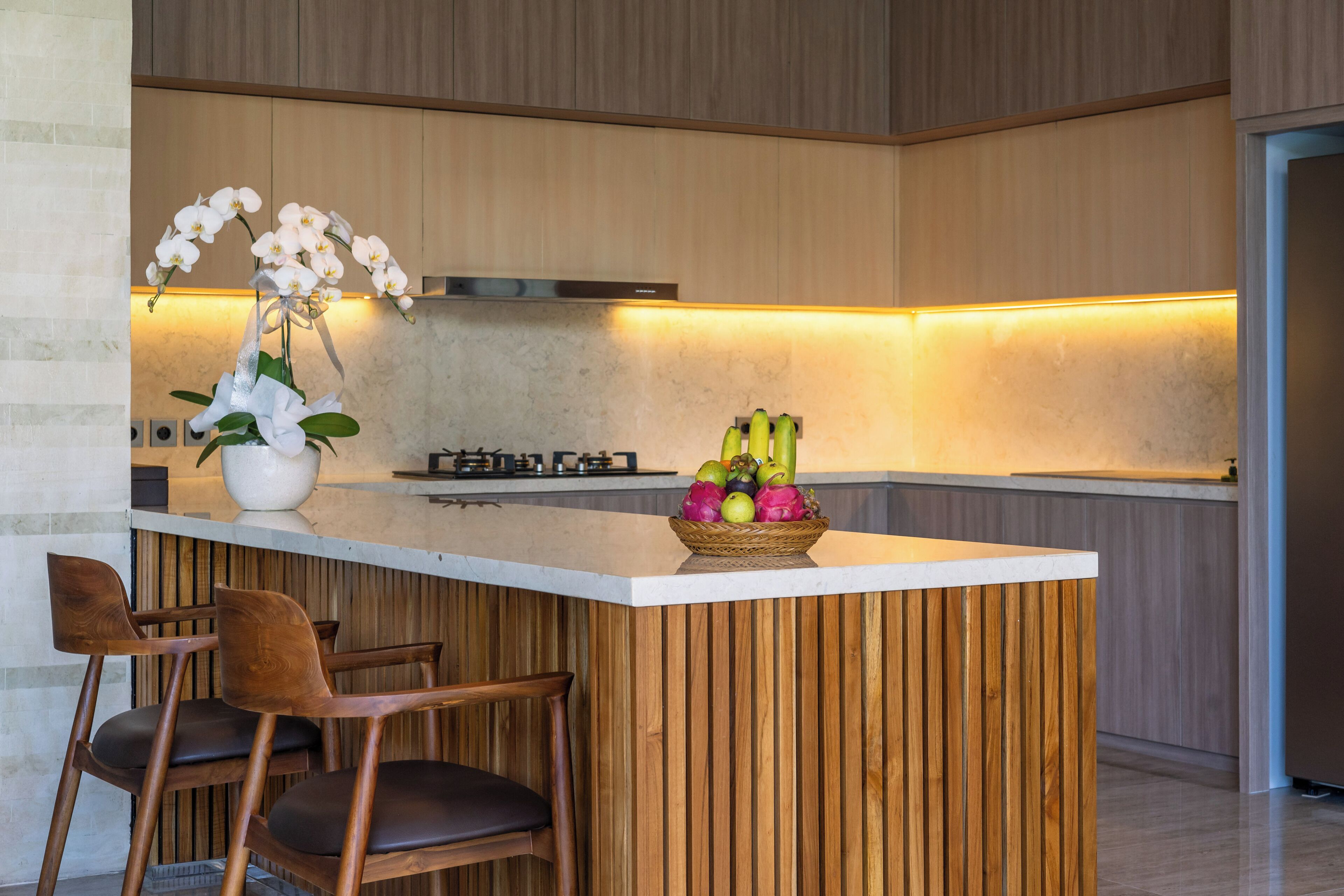 Cocina moderna con una isla de madera, taburetes de bar, un frutero y un centro de mesa con orquídeas.