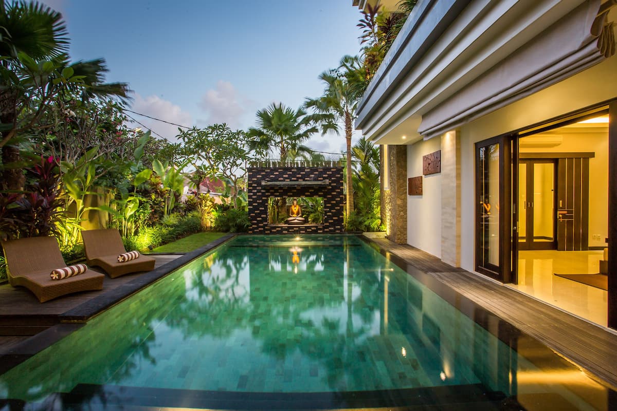 A swimming pool with lounge chairs, surrounded by tropical plants and a stone archway.