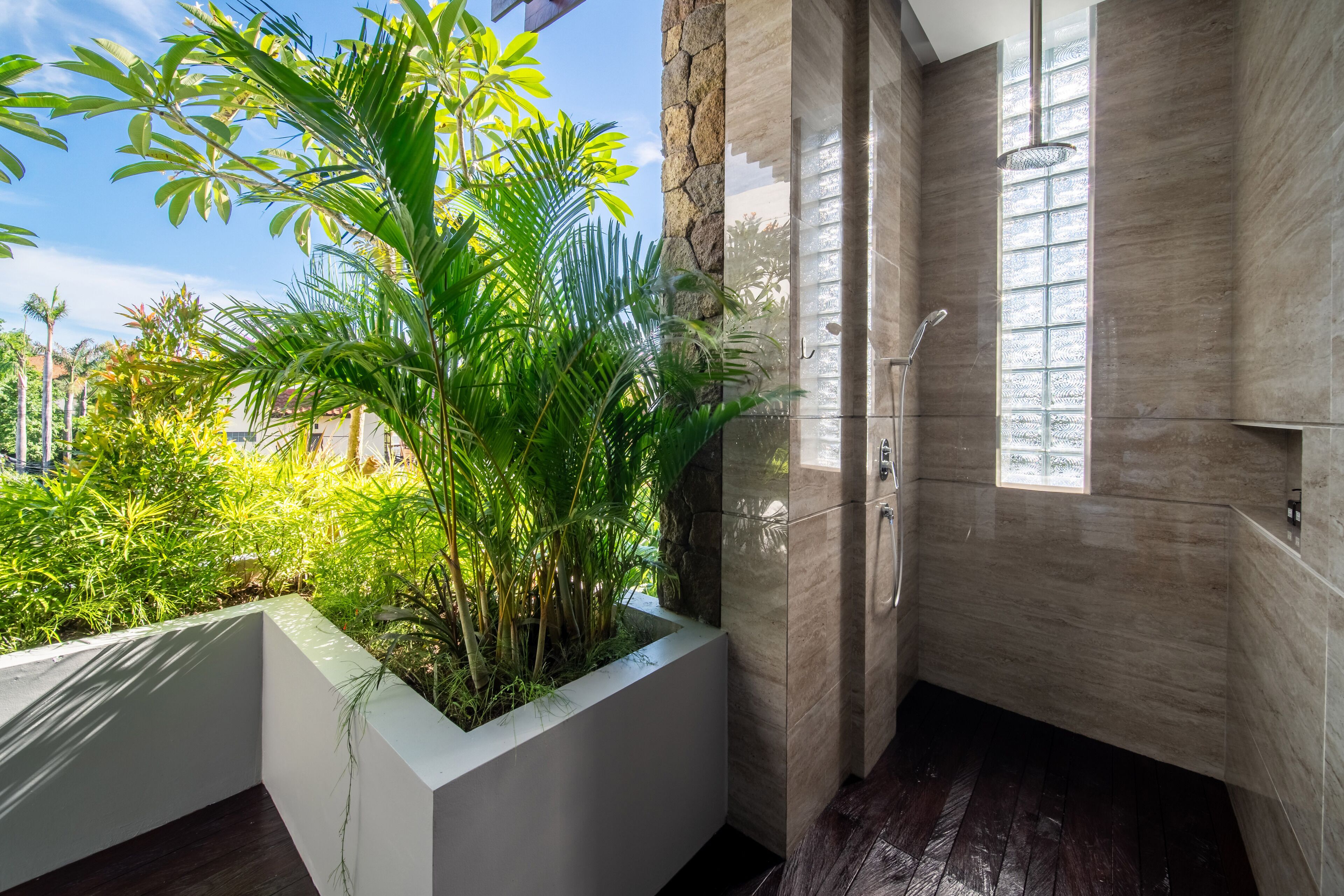 Une salle de bain moderne dotée d’une grande fenêtre, d’une douche et d’un bac à plantes contenant des plantes tropicales.