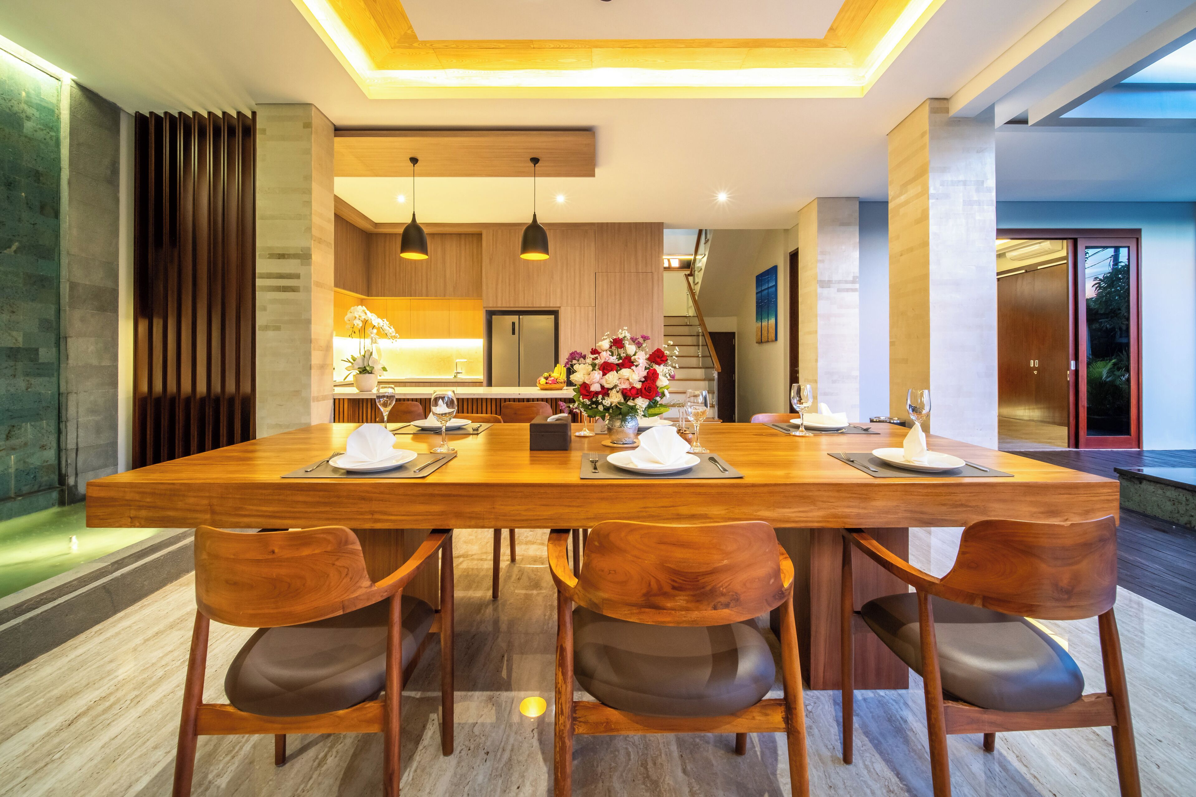 A modern dining area with a wooden table, four chairs, and a kitchen in the background.