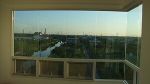 A room with a large window overlooking a water body and industrial structures. - At Ease Hotel Suvarnabhumi (Bang Phli)