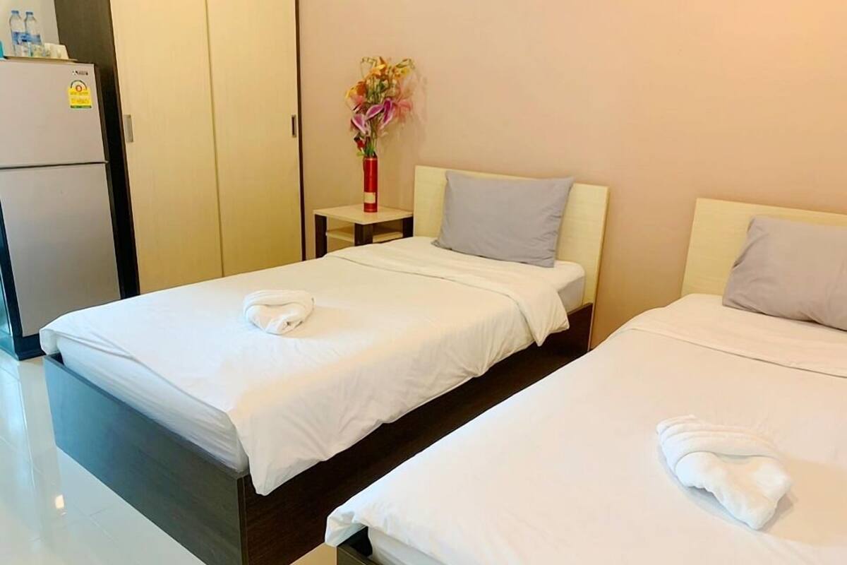 Une chambre d’hôtel avec deux lits, chacun étant équipé de draps et de serviettes blancs. Une petite table avec un vase de fleurs se trouve entre les deux lits.