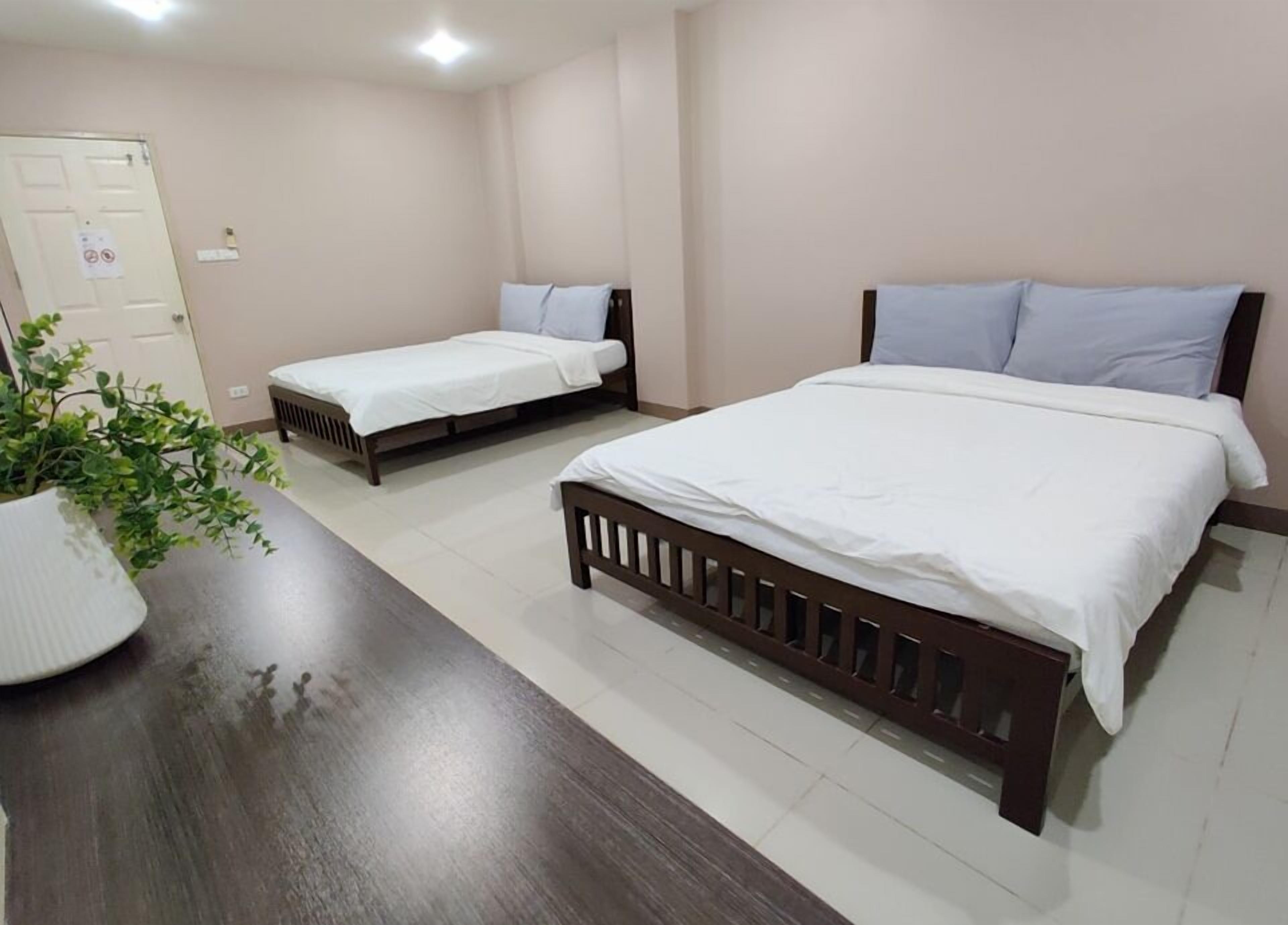 A hotel room with two beds, a wooden desk, and a potted plant.
