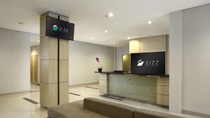 A modern hotel lobby with a reception desk, a sofa, and a potted orchid. - Zizz Convention Hotel (Dalung)