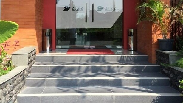 A modern building entrance with a red facade, a glass door, and a set of stone steps leading up to it. - Zizz Convention Hotel (Dalung)