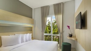 A hotel room with a large bed, a TV mounted on the wall, a window with curtains, and a small potted plant on a shelf. - Zizz Convention Hotel (Dalung)