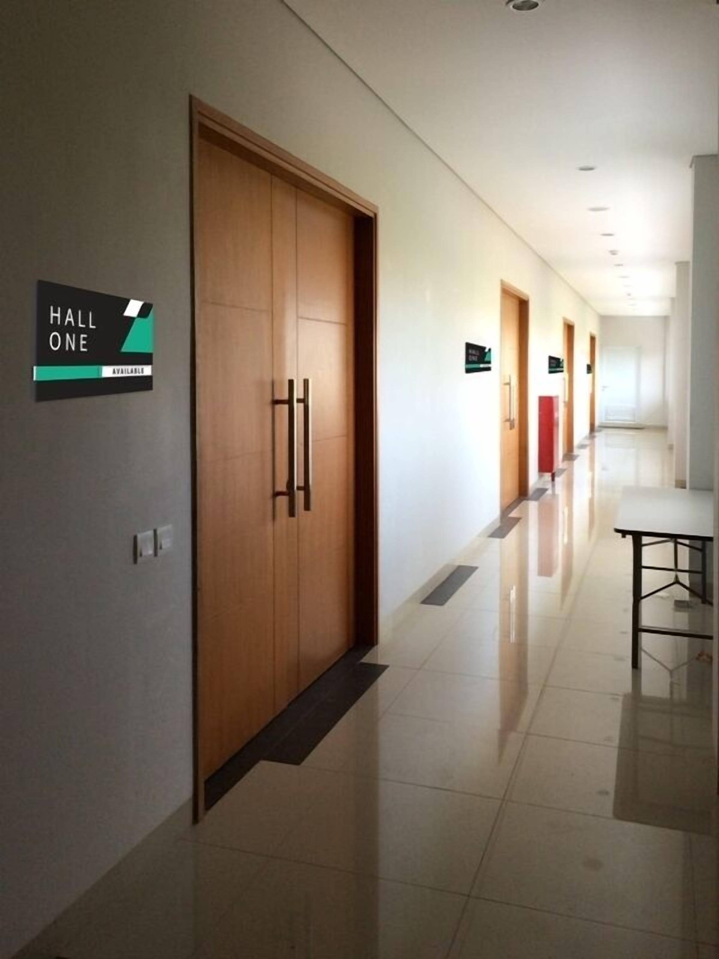 A hotel hallway with wooden doors, a sign indicating 'Hall One' is available, and a table on the right.