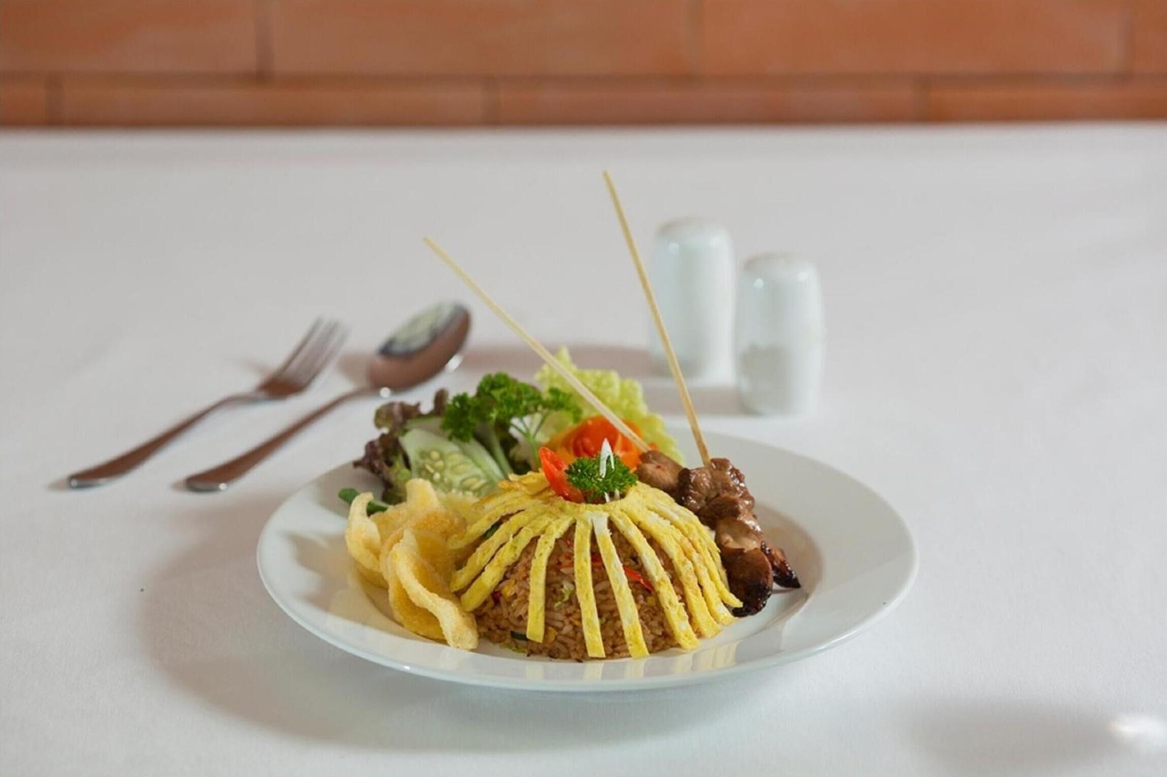 A plate of fried rice topped with meat and vegetables, accompanied by a side salad and a small portion of fried wonton.