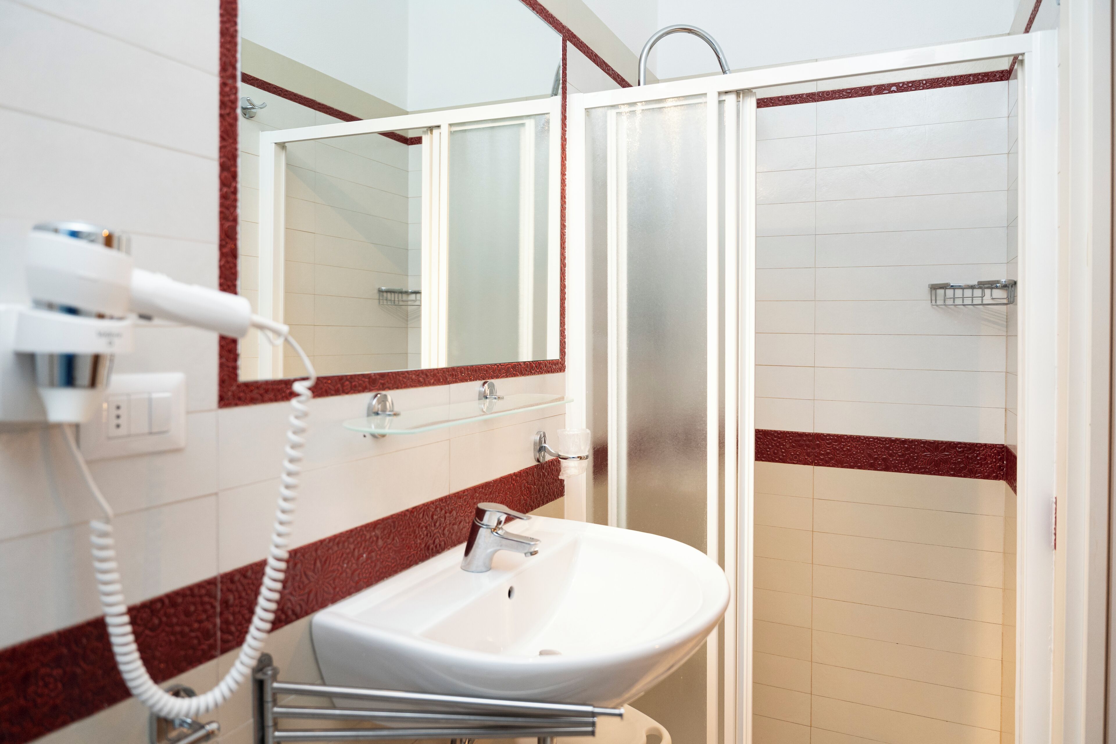 Un baño con un lavamanos blanco, cabina de ducha con paredes de vidrio y un espejo con dos paneles de vidrio.