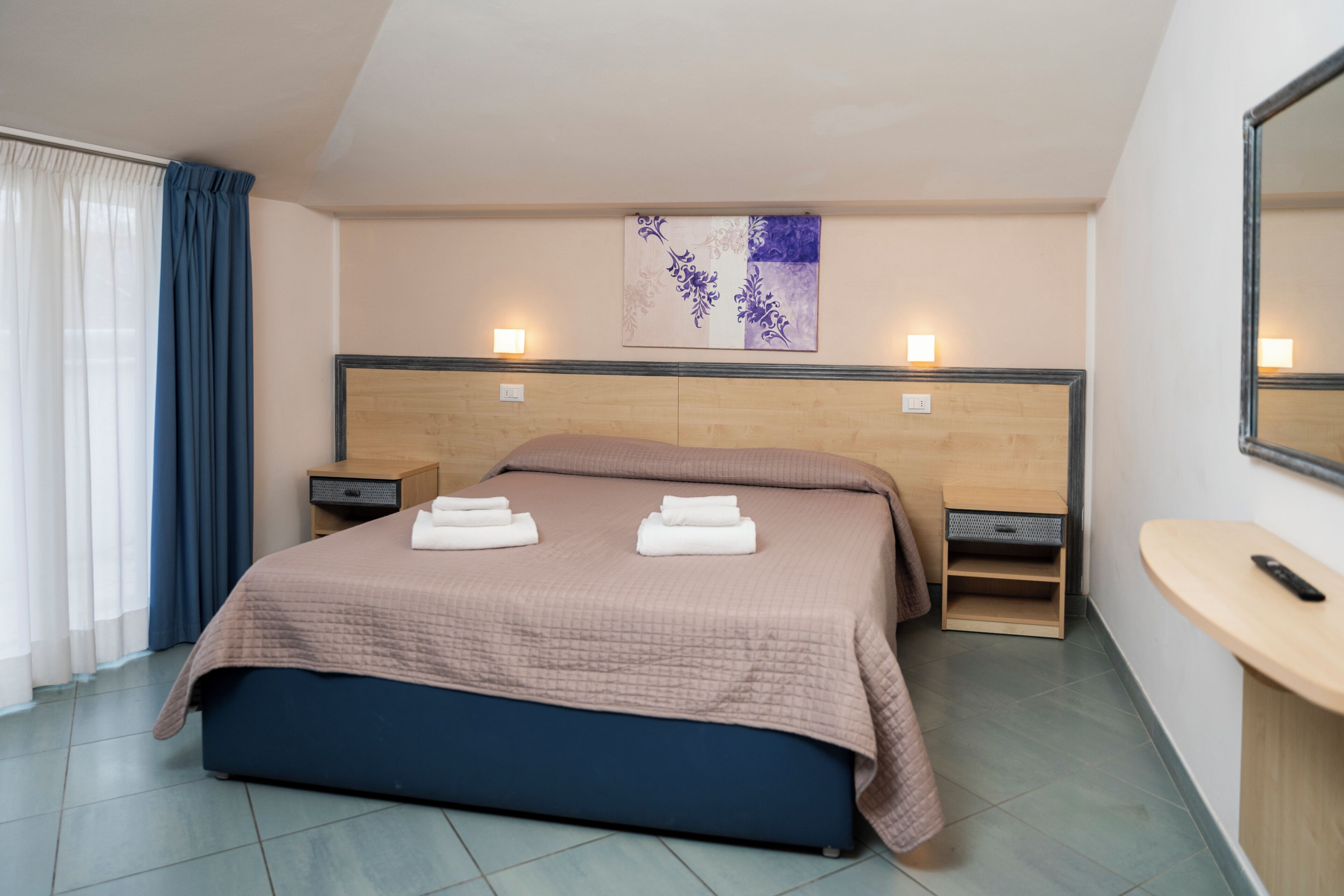A neatly made bed with a headboard, bedside tables, a wall-mounted artwork, and a small wooden stool.