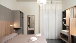 Een hotelkamer met een bed, een spiegel, een badkamer met wastafel en een douche.
