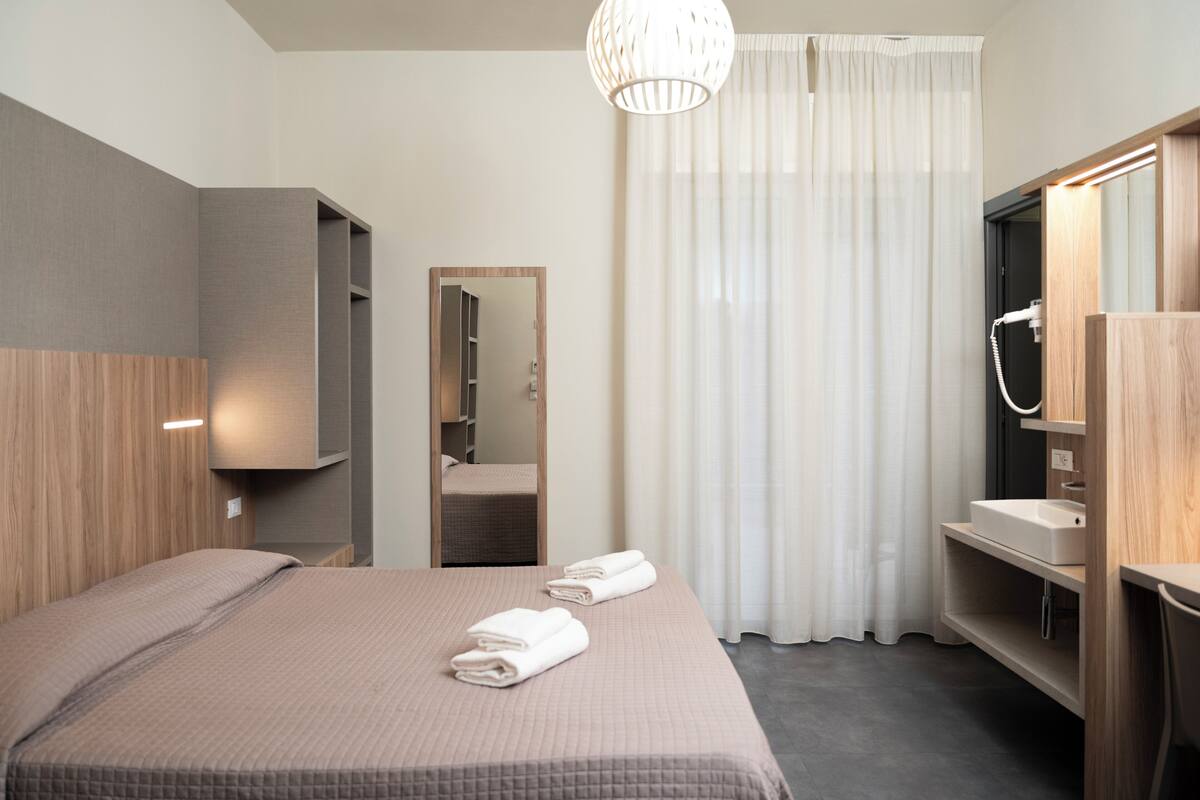 A hotel room with a bed, a mirror, a bathroom with a sink, and a shower.