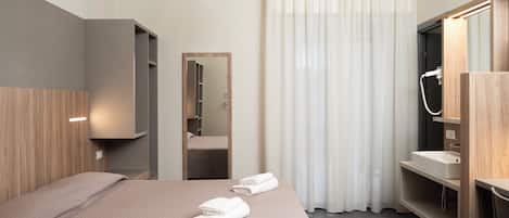 Una habitación de hotel con cama, espejo, baño con lavamanos y ducha.