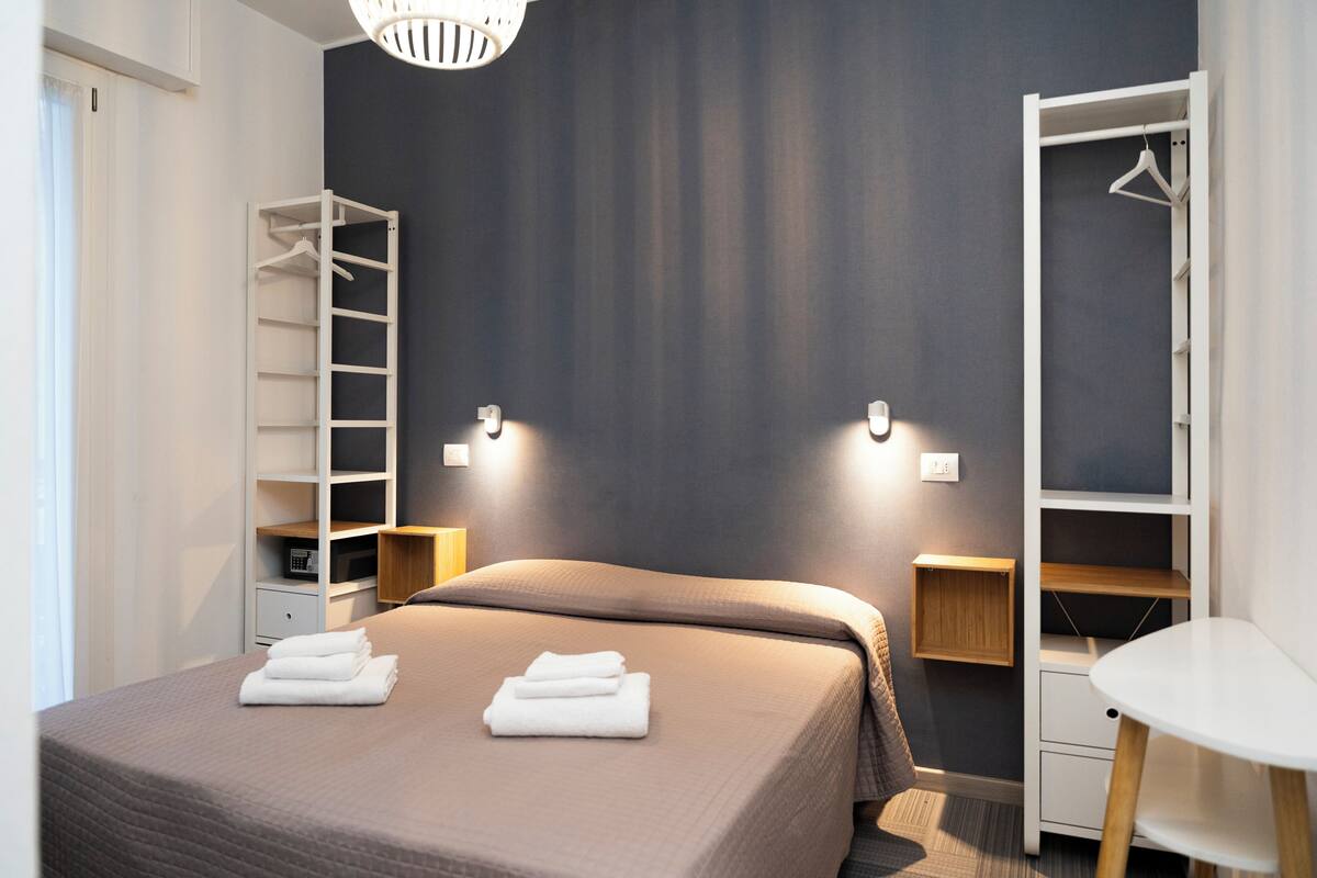 A bedroom with a bed, a wardrobe, a bedside table, and a hanging light fixture.