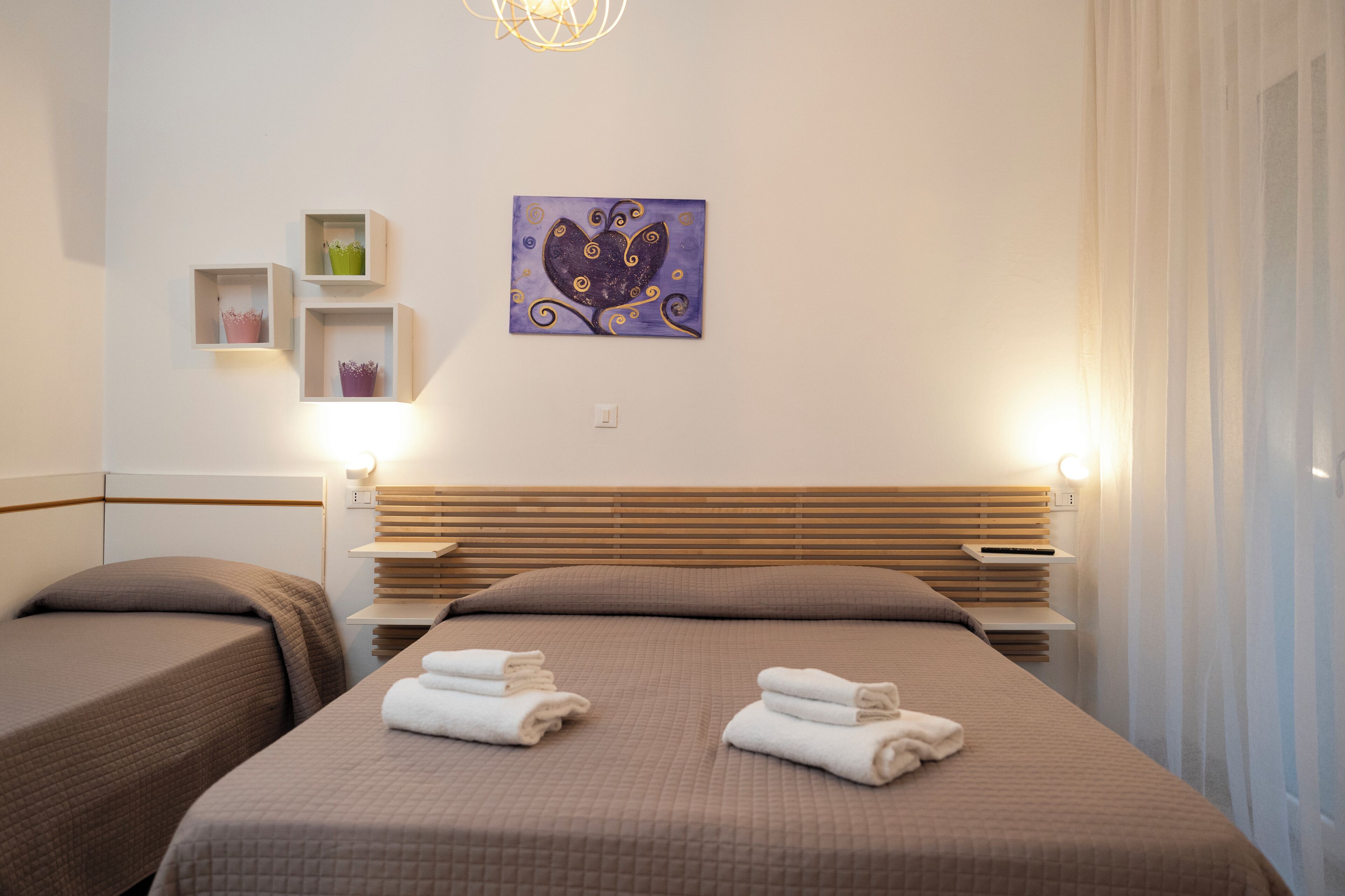 Una habitación de hotel con dos camas, una obra de arte en la pared y mesitas de noche con lámparas.