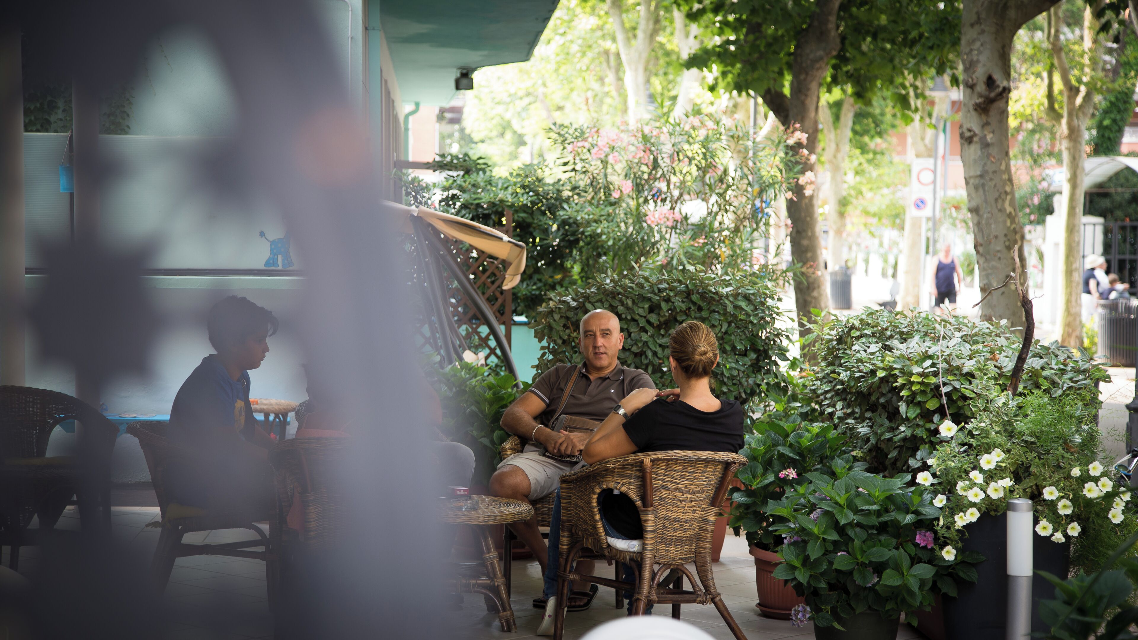 An outdoor seating area with wicker chairs, potted plants, and a shaded table.