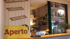 Een bar met houten borden waarop verschillende soorten alcohol staan aangegeven, een geel bord met de tekst 'Aperto' en gevulde flessenkasten.
