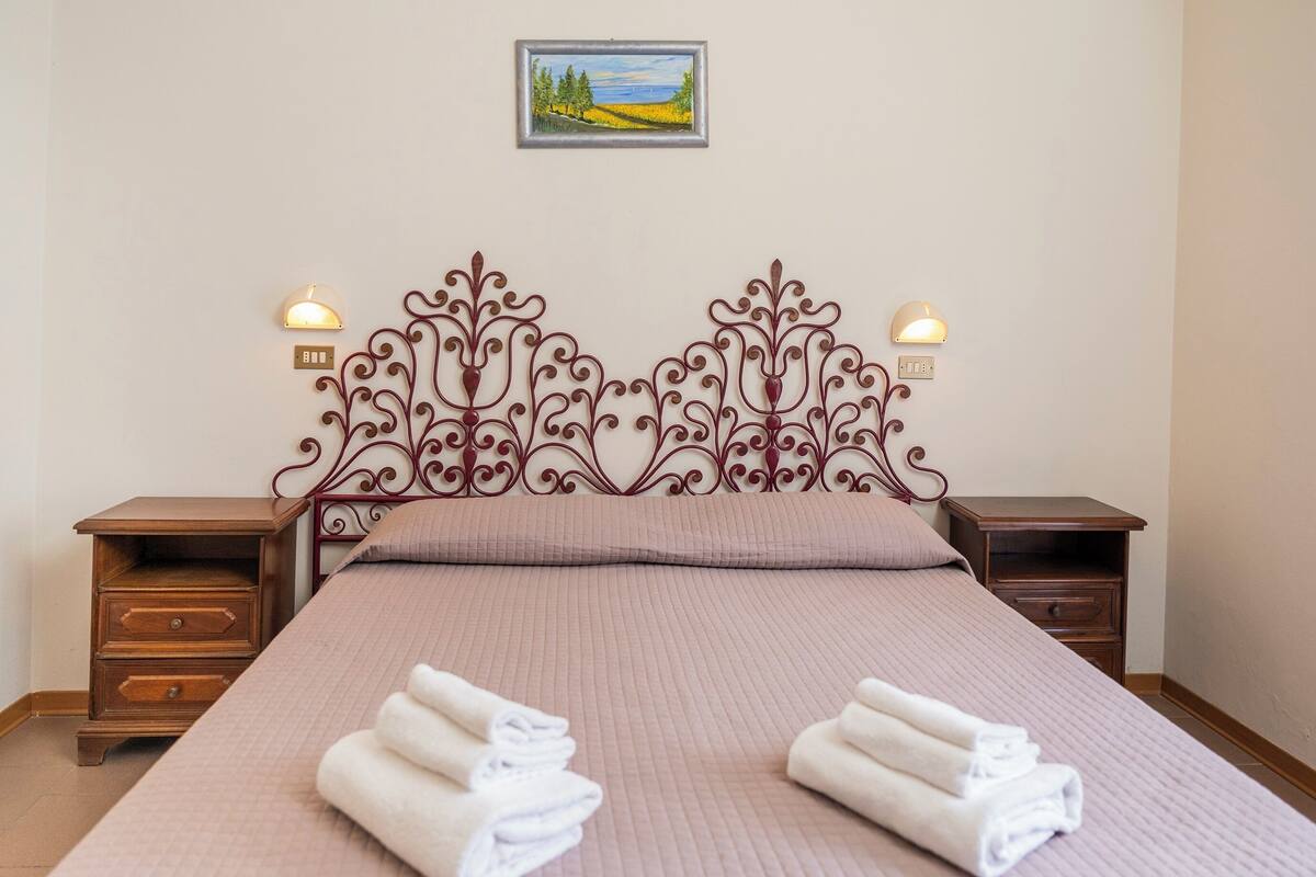 A neatly made bed with a decorative headboard, two bedside tables, and a wall-mounted painting.