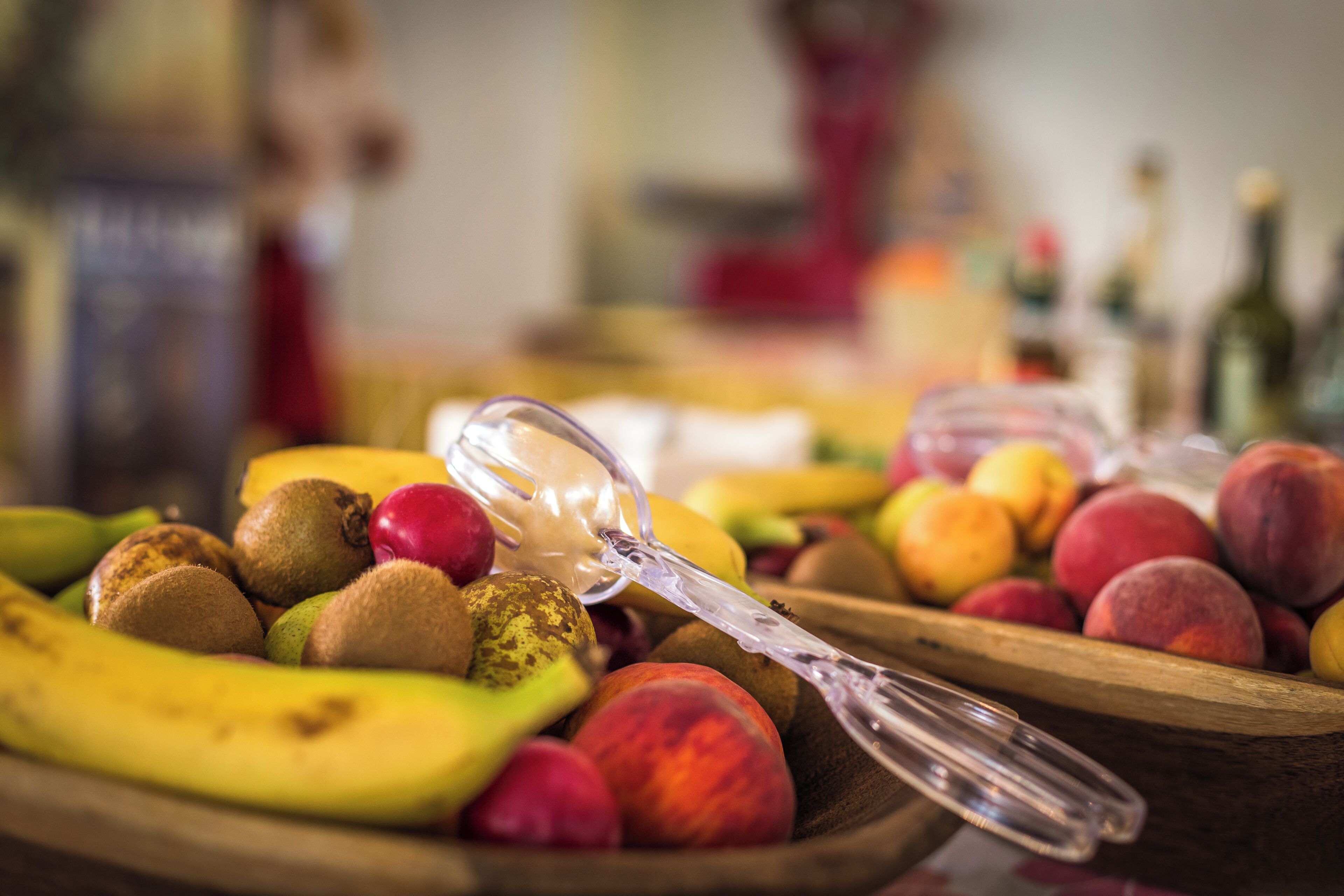 A wooden fruit bowl with a variety of fruits including bananas, kiwis, and peaches.