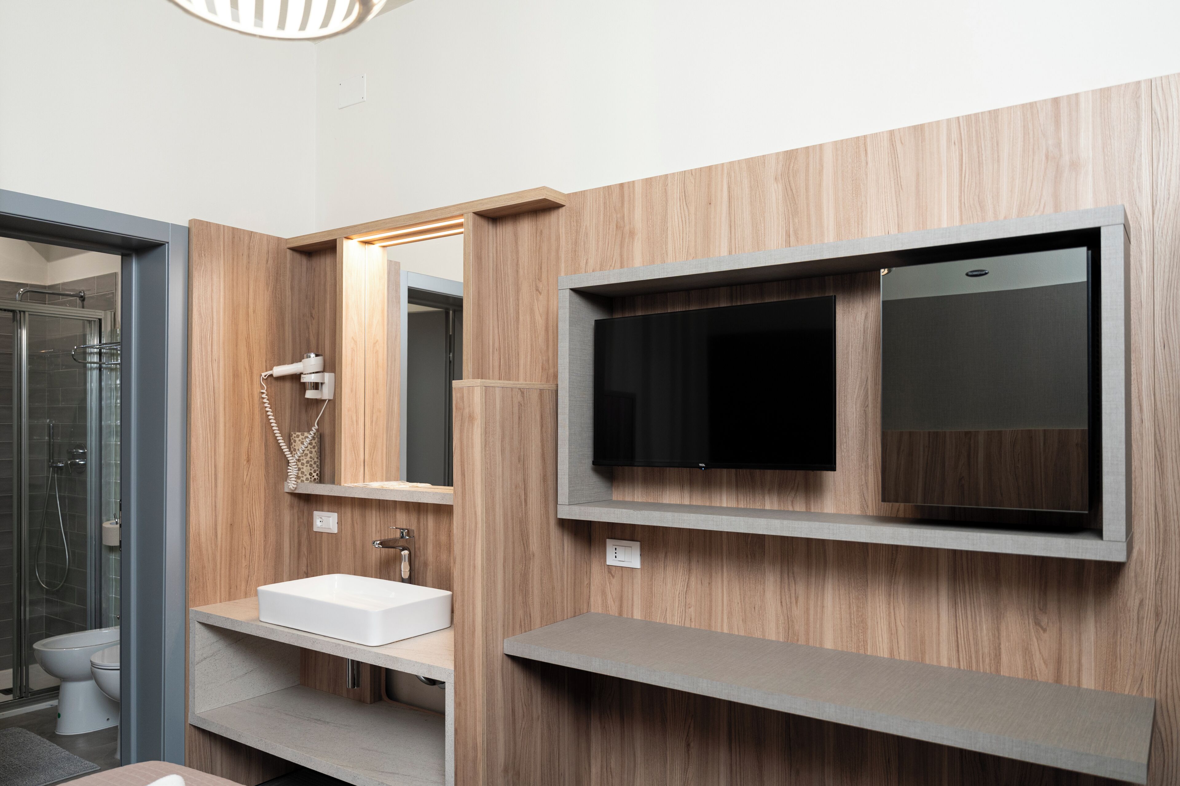 Une salle de bain moderne avec un meuble-lavabo en bois, un grand miroir et un téléviseur encastré.