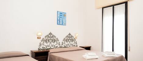 Habitación de hotel con dos camas, un cabecero decorativo, lámparas de noche, un cuadro en la pared y una puerta corredera a la derecha.