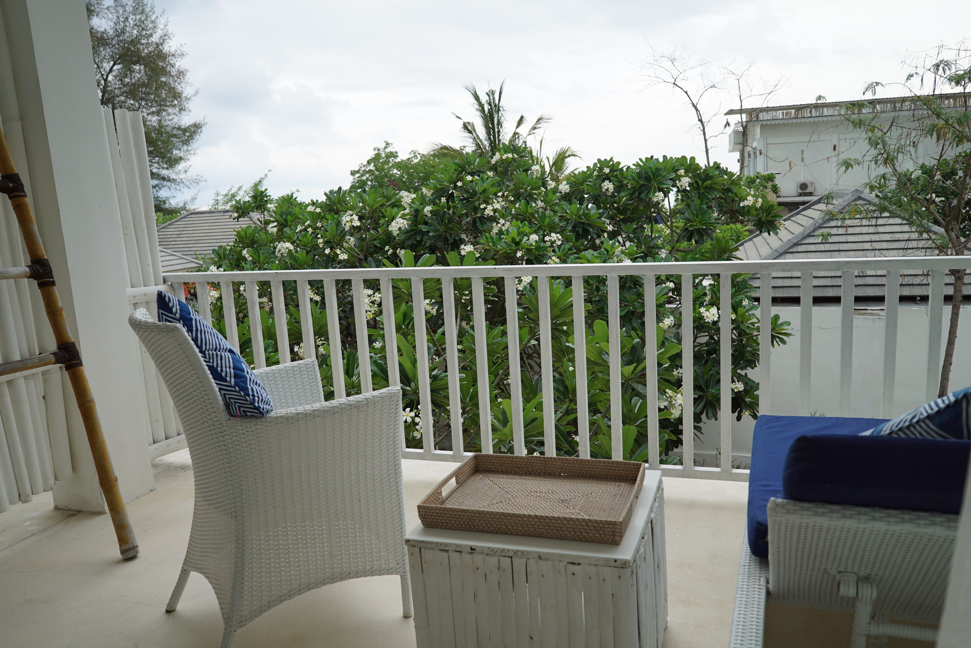 A balcony with wicker furniture, a white railing, and lush greenery in the background.