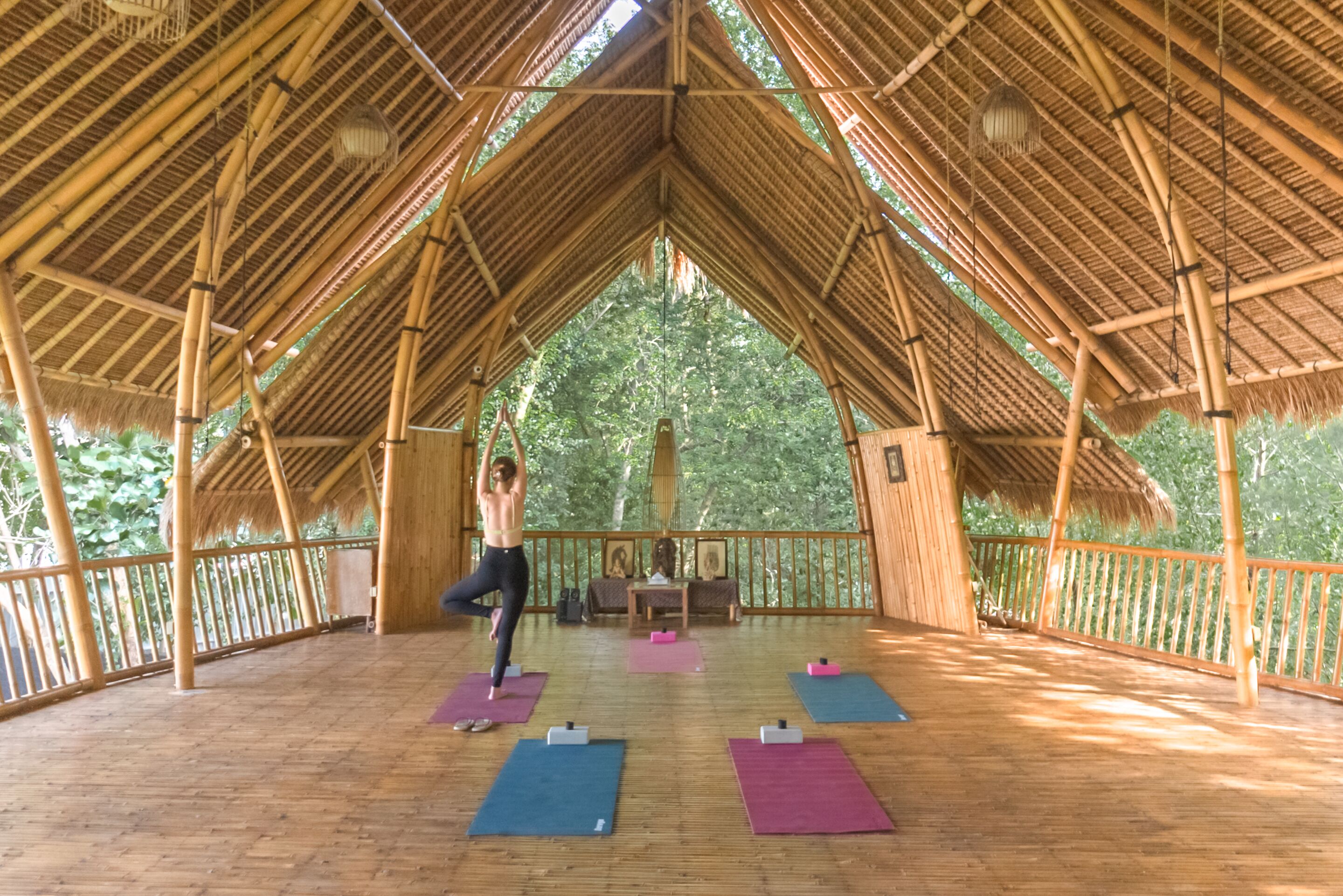 Un estudio de yoga con techo de paja, piso de madera y colchonetas de yoga.
