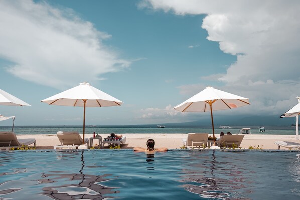 A swimming pool with lounge chairs and umbrellas, overlooking a beach and ocean.