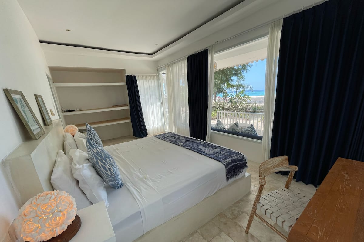Un dormitorio con cama, mesita de noche, silla y vistas al exterior.