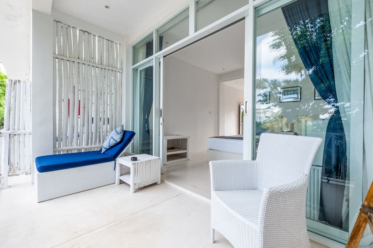 Un moderno salón con un sofá de mimbre blanco, un sillón azul acolchado y una pequeña mesa blanca.