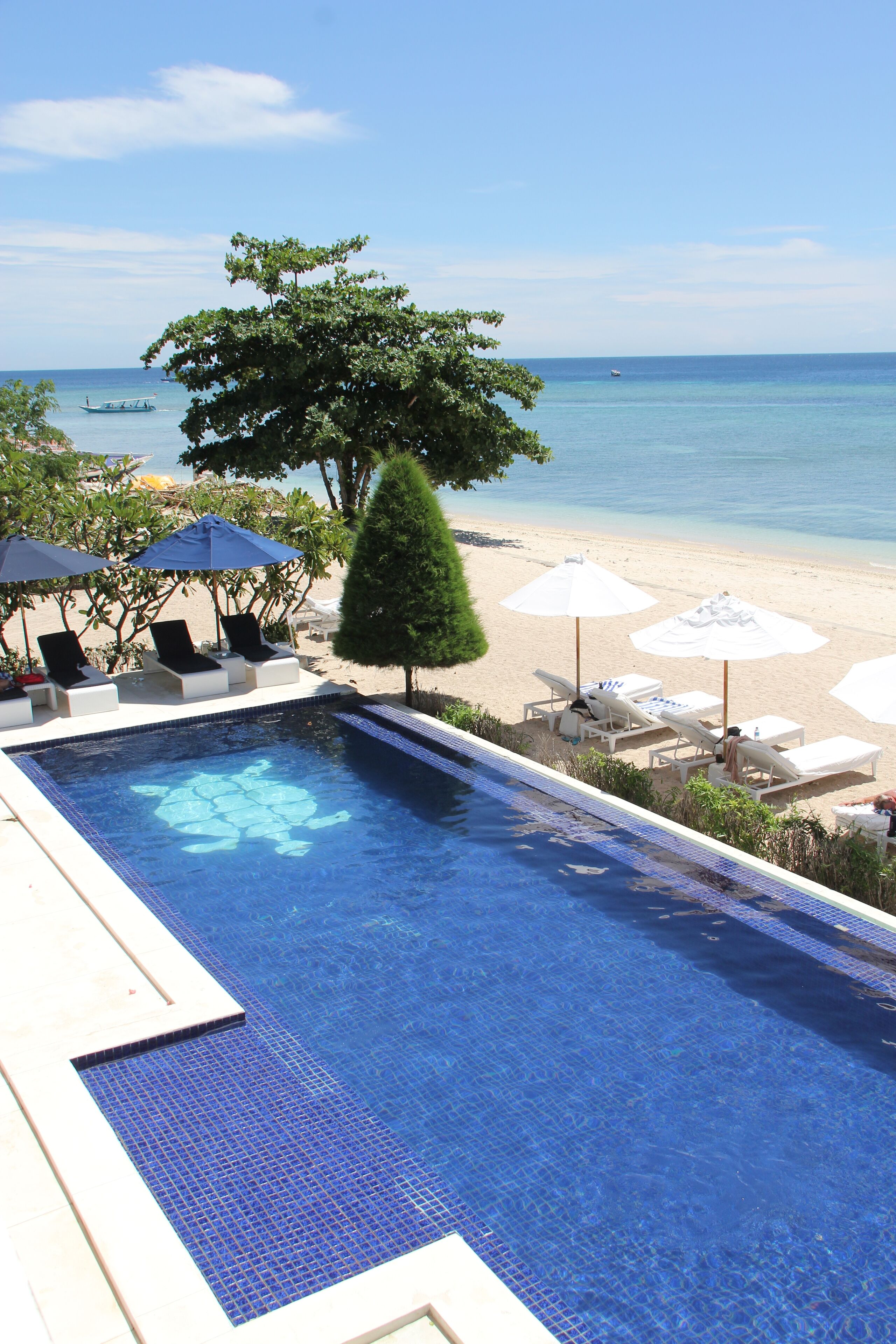 A swimming pool with lounge chairs and umbrellas, a beach, and a view of the ocean.