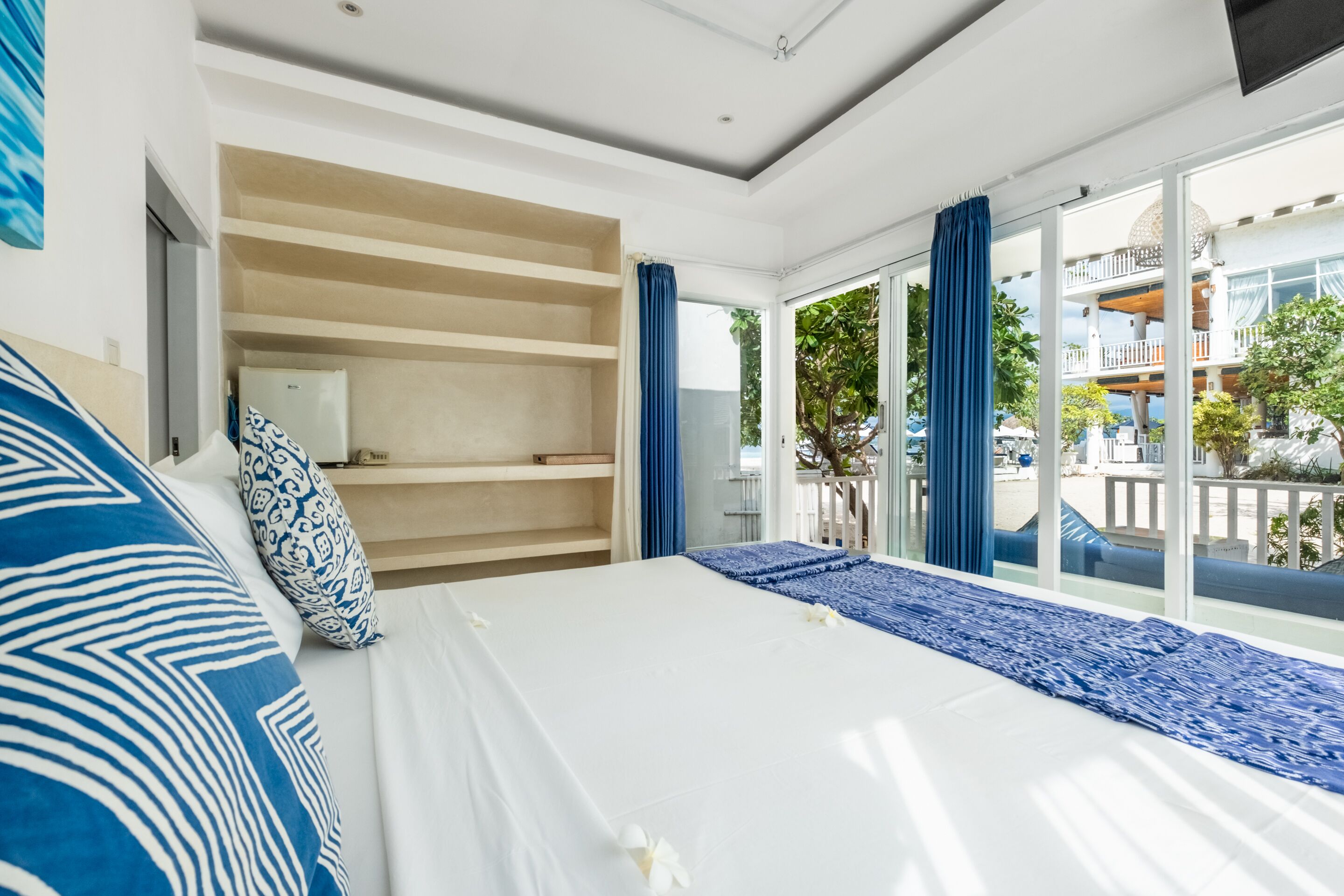Une chambre d’hôtel moderne dotée d’un grand lit, d’une armoire intégrée et d’un balcon offrant une vue sur le complexe hôtelier.