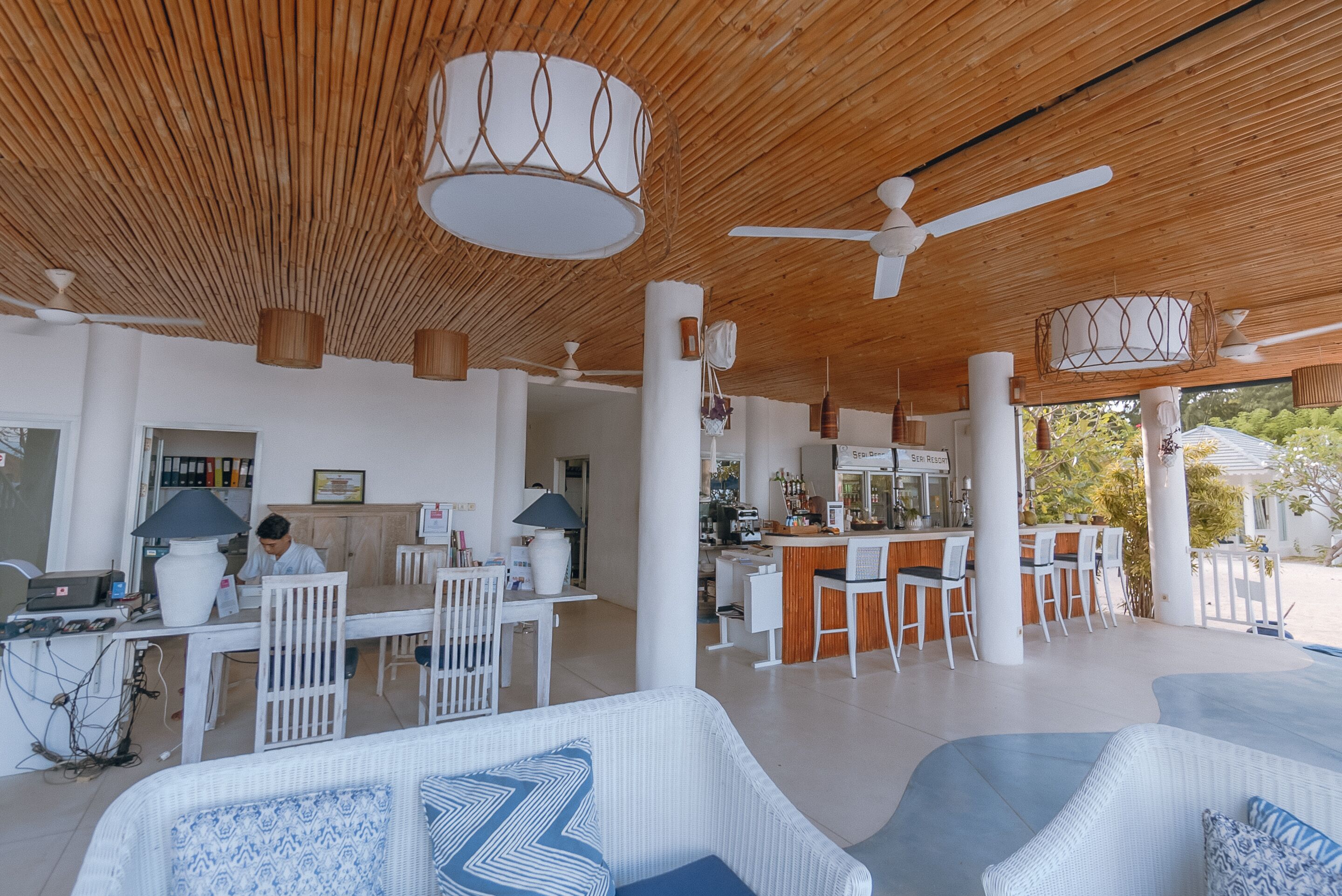 A spacious indoor area with a wooden ceiling, white furniture, and a bar area.