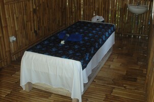 Una cama individual con una colcha blanca y azul estampada con flores, un mantel blanco y un suelo de madera.