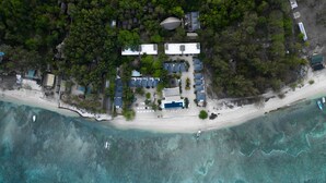 Vue aérienne d’un complexe hôtelier situé sur la côte, avec de nombreux hébergements de type bungalow, un espace piscine central et une plage.