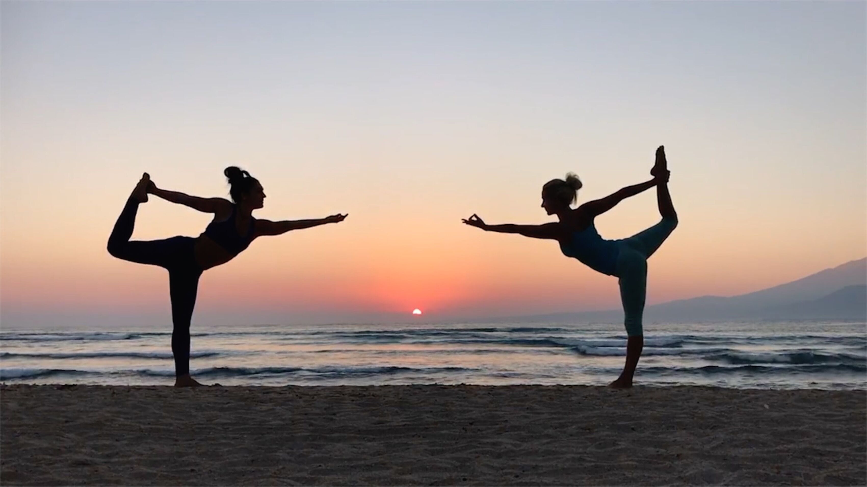 Two individuals performing yoga on a beach at sunset.