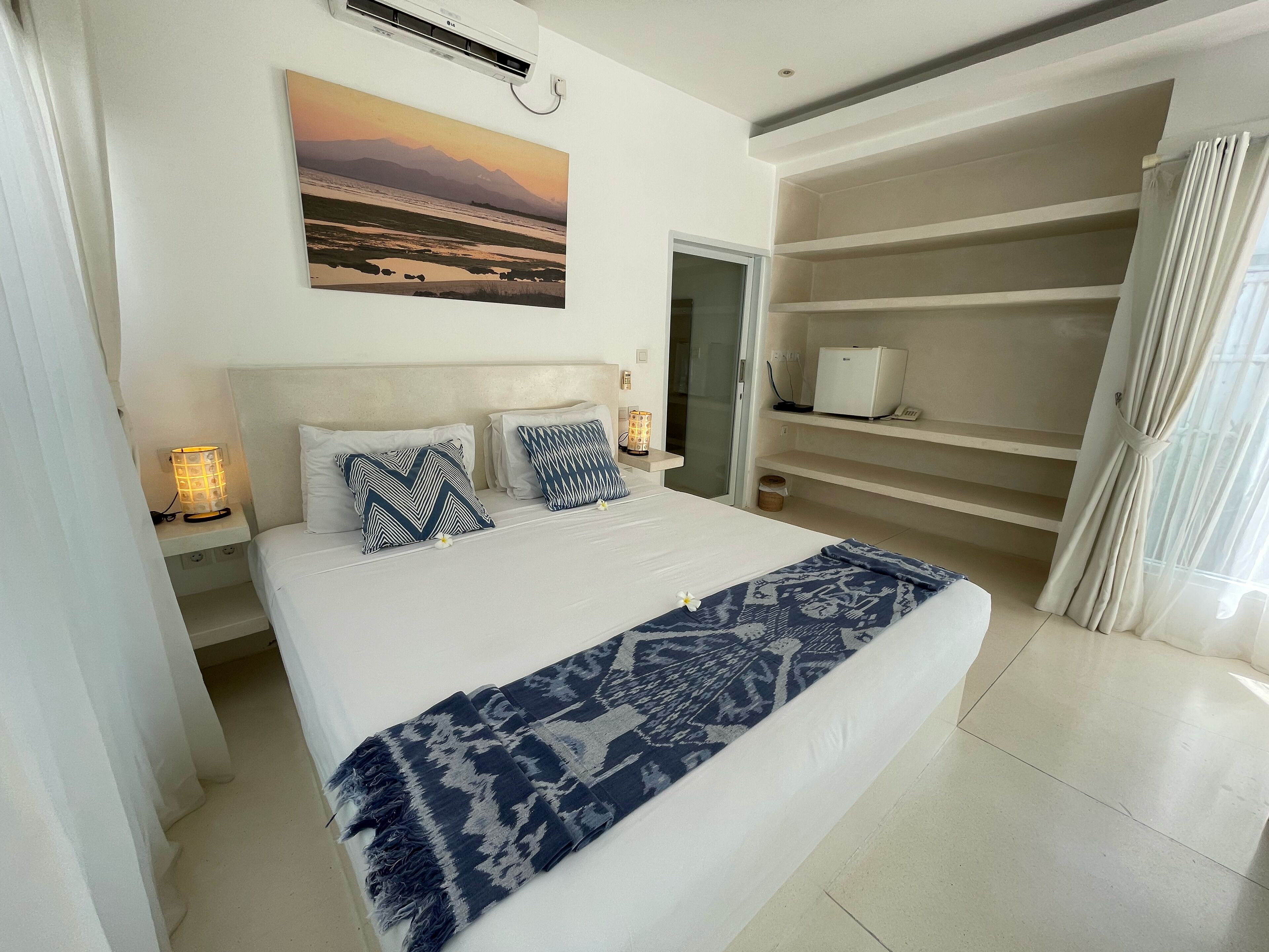 A bedroom with a bed, a nightstand with a lamp, a painting on the wall, and a wardrobe.