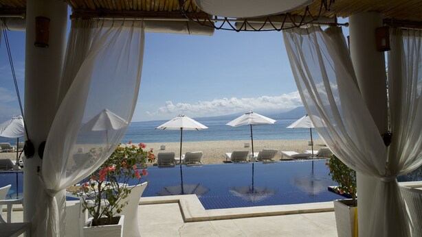 Une piscine à débordement bordée de parasols blancs et de chaises longues, offrant une vue sur la plage et la mer.