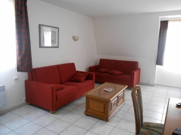 A living room with two red sofas, a wooden coffee table, and a dining table with chairs.