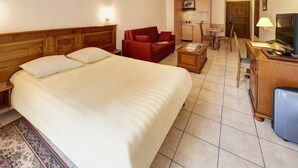 Habitación de hotel con una cama grande, un sofá rojo, un escritorio con televisor y una kitchenette pequeña.