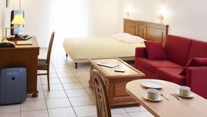 Una habitación de hotel con una cama, un sofá rojo, un escritorio de madera con una lámpara, una silla y una pequeña mesa con tazas y platos.