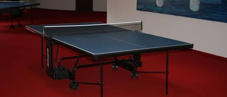 A ping pong table in a room with a red carpet and a painting of a bridge on the wall.