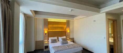 A hotel room with a large bed, bedside lamps, a headboard with built-in lighting, a carpeted floor, and a door leading to a bathroom.