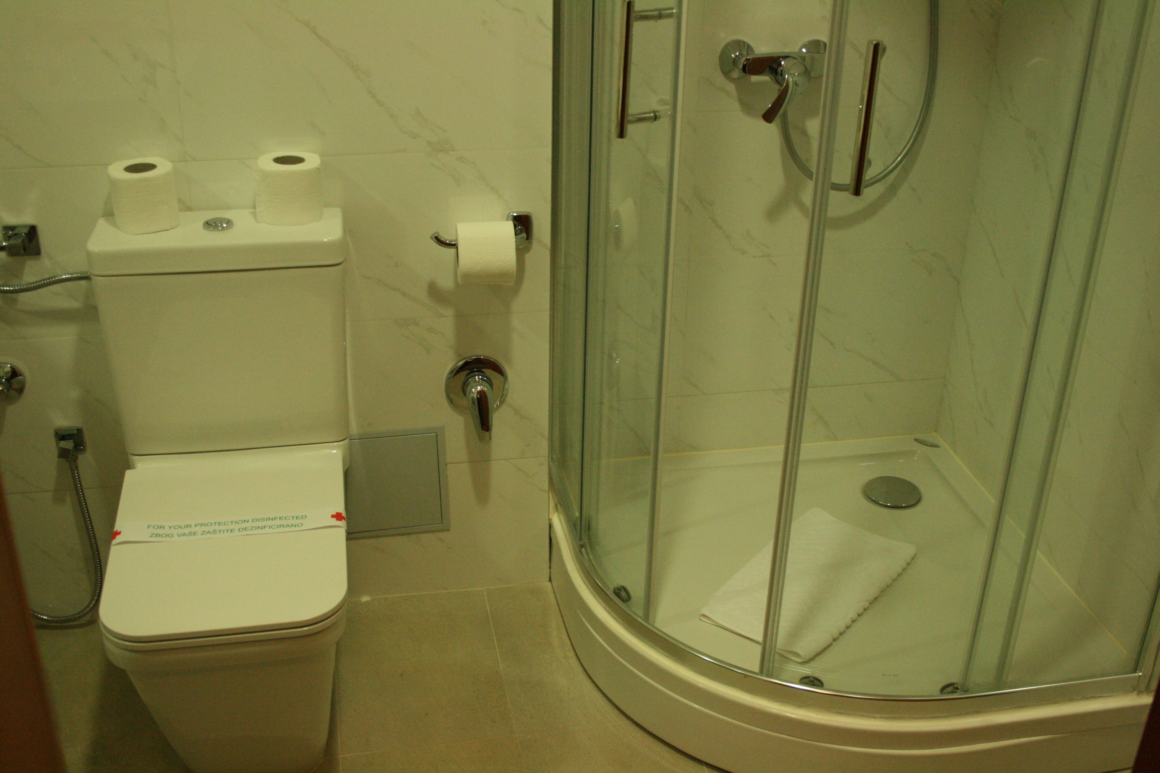 A bathroom with a toilet, a glass-enclosed shower, and a marble-tiled wall.