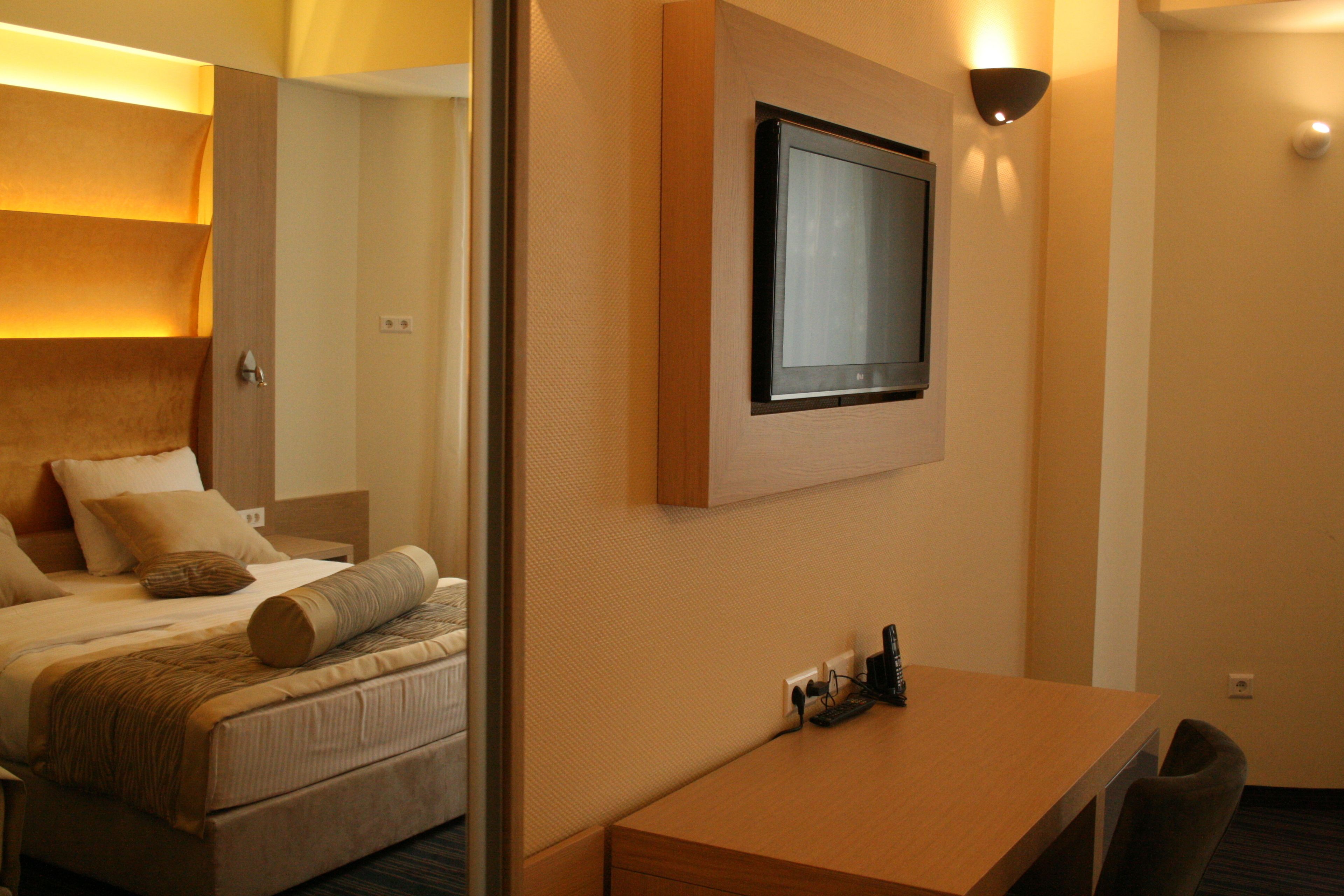 Una habitación de hotel con cama, mesita de noche y televisor de pared.