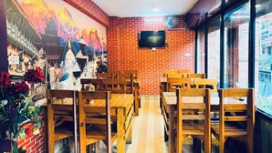 Ein Restaurant mit Ziegelwänden, Holztischen und -stühlen, einem Wandgemälde und einem Fernseher.