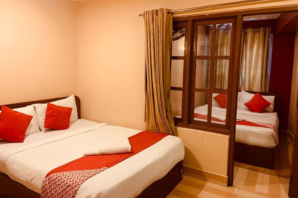 A hotel room with a large bed, a smaller bed, and a window with curtains.