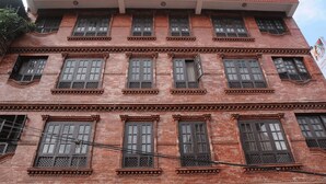 Ein mehrstöckiges Gebäude mit roter Backsteinfassade, zahlreichen Fenstern mit dekorativen Gitterrosten und einem Flachdach.