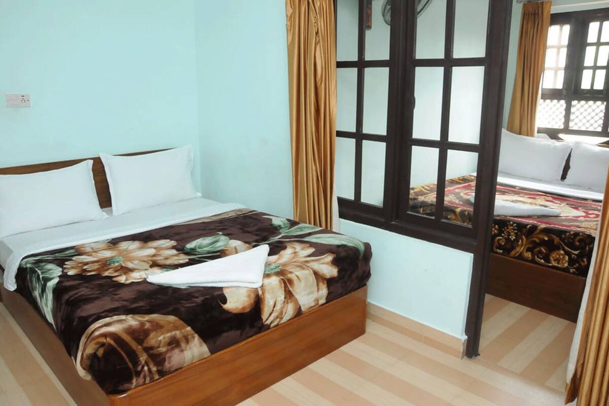 A room with a bed, a window with curtains, and a second bed in the background.